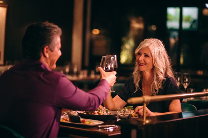 Couple toasting to each other in dark lit restaurant for date night in grande prairie