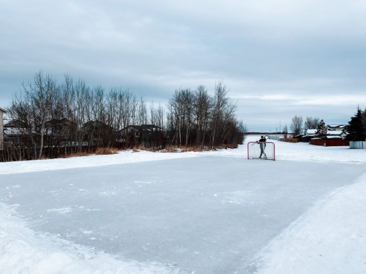 A community skating rink with a hockey net and one skater. 