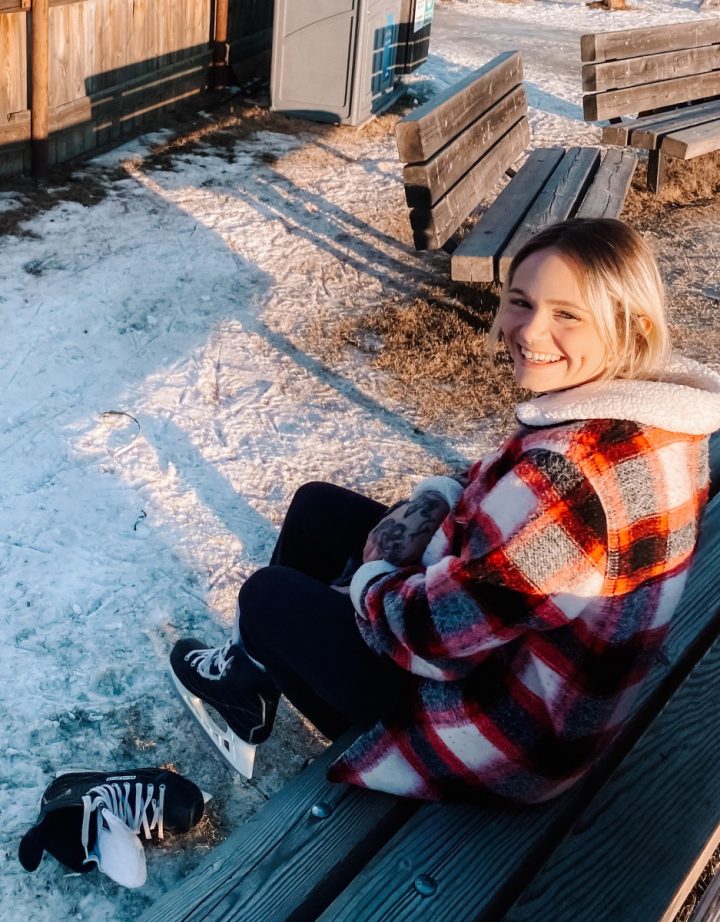 A woman sitting on a bench and putting on a pair of hockey skates.