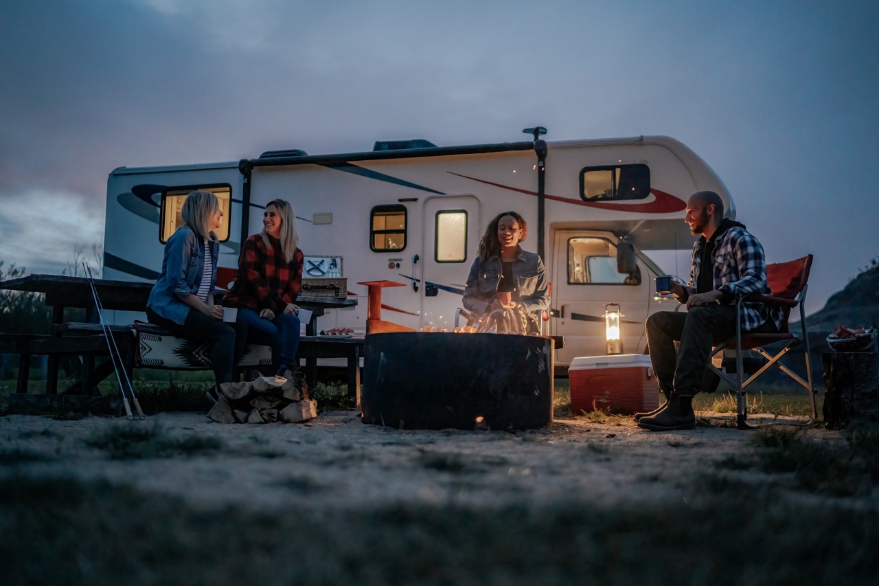 People sitting around a campfire at night with a motorhome in the background